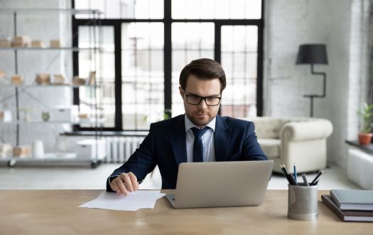 Man in a suit sitting at a desk looking at a laptop as a trusted advisor.